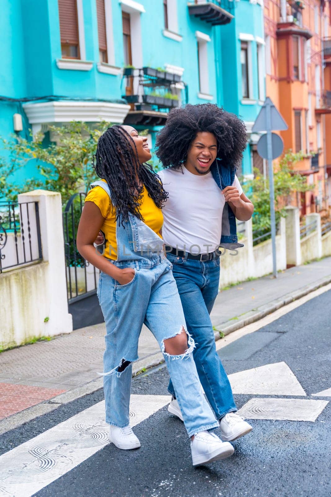 Vertical photo of young african lovers walking embraced along a street with colorful houses