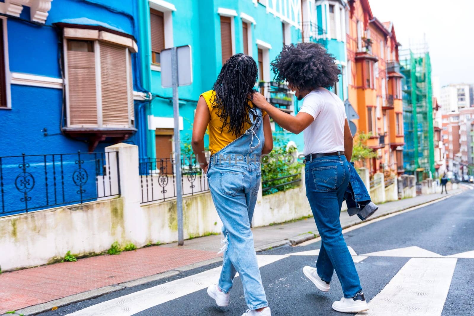 Rear view of two african american young friends walking along a colorful street