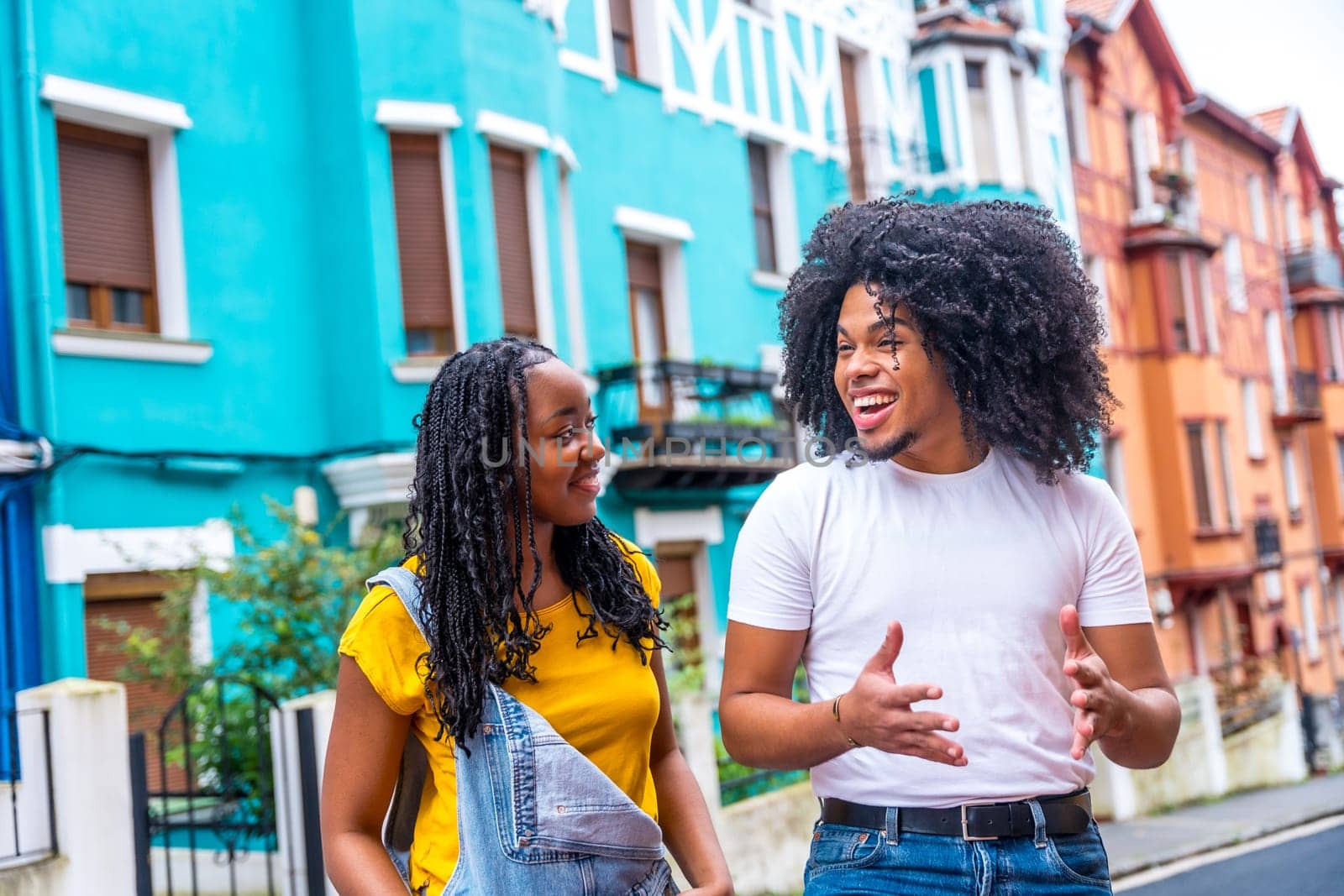 Two happy young african friends talking while visiting a city street with colorful houses