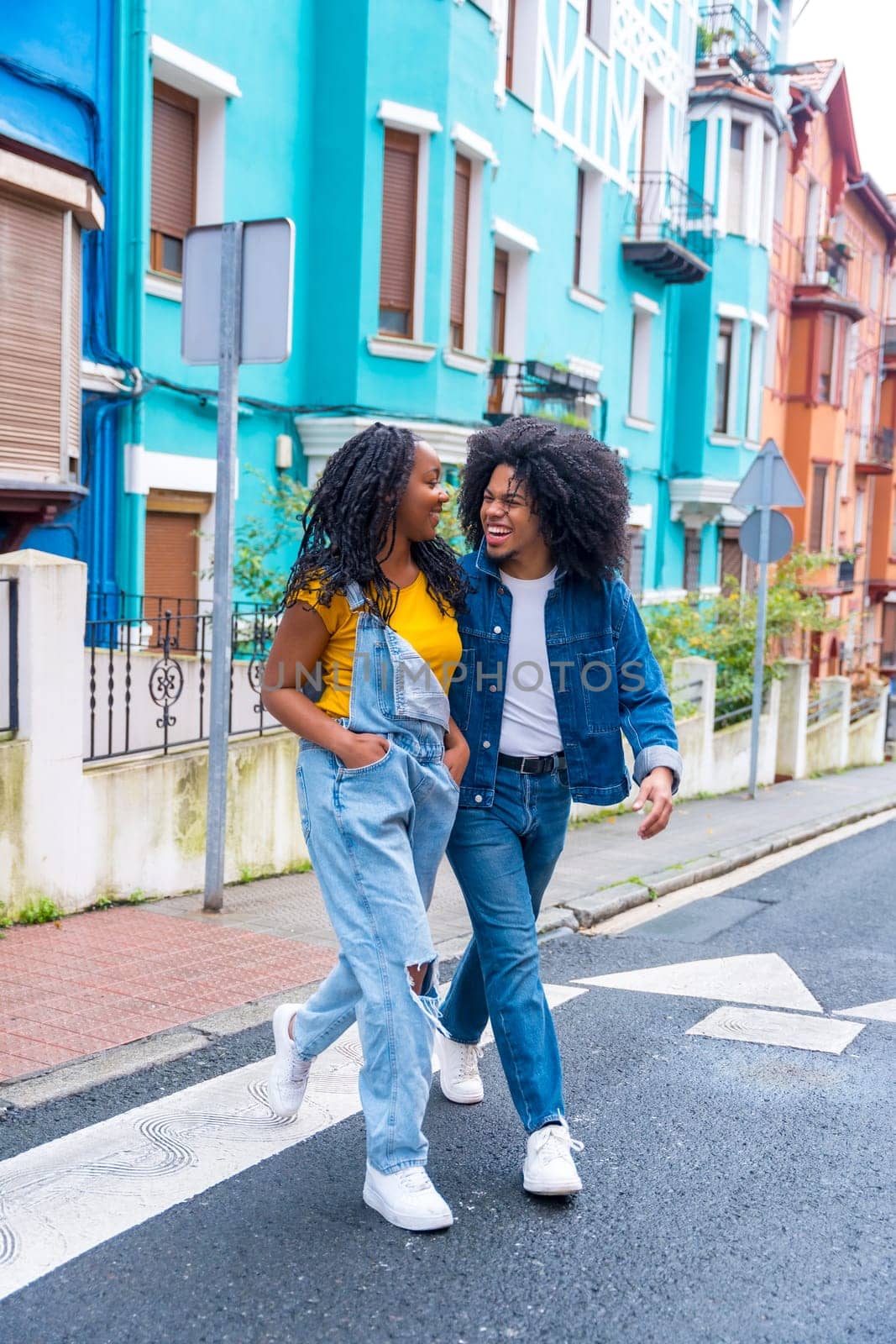 Vertical photo of a young african american couple walking together along a street with colorful facades