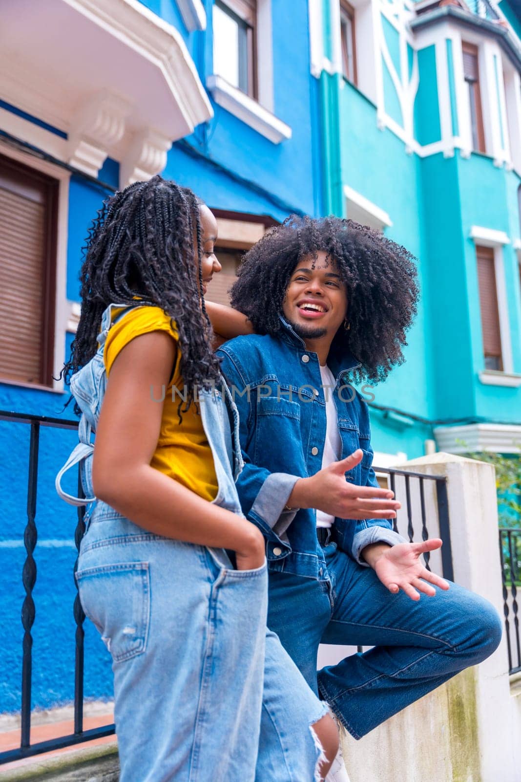 Vertical photo of two african american friends chilling and talking outside a blue colorful house
