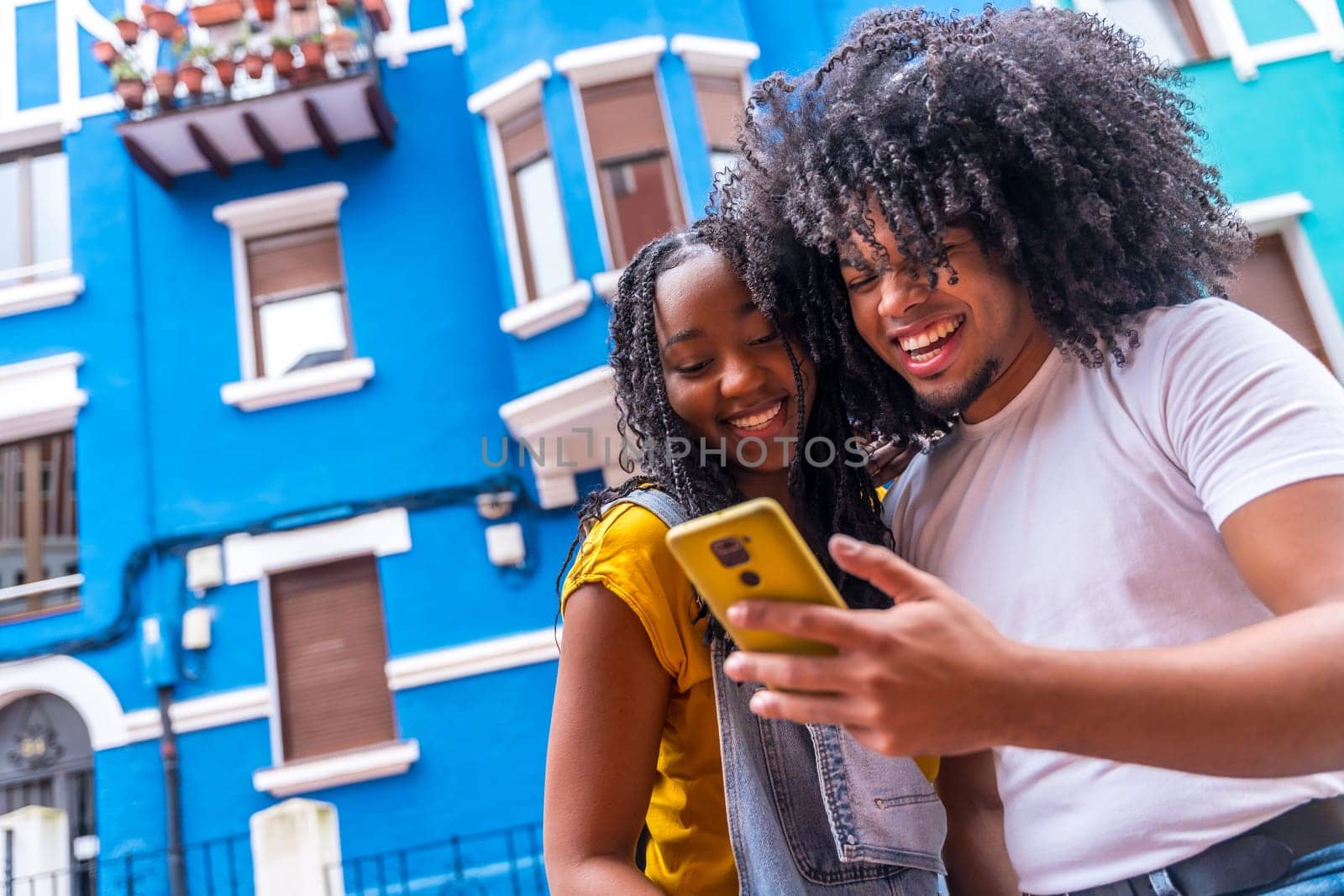 Low angle view portrait with copy space of a young african friends using phone standing in the street with blue colorful houses