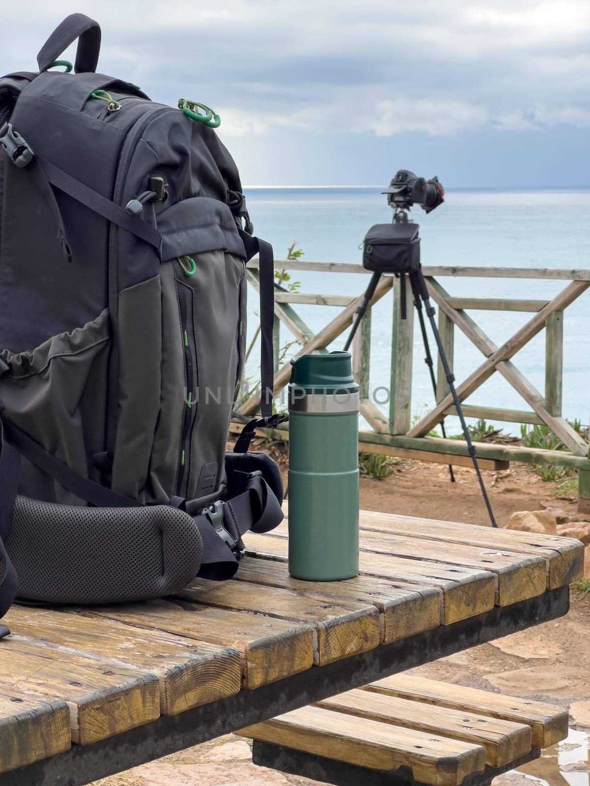 Photo backpack and thermos lie on the table in front of the camera by Sonat