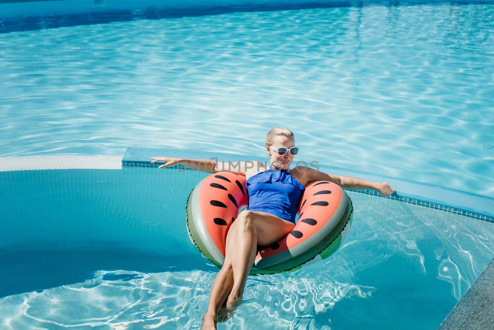 Happy woman in a swimsuit and sunglasses floating on an inflatable ring in the form of a watermelon, in the pool during summer holidays and vacations. Summer concept