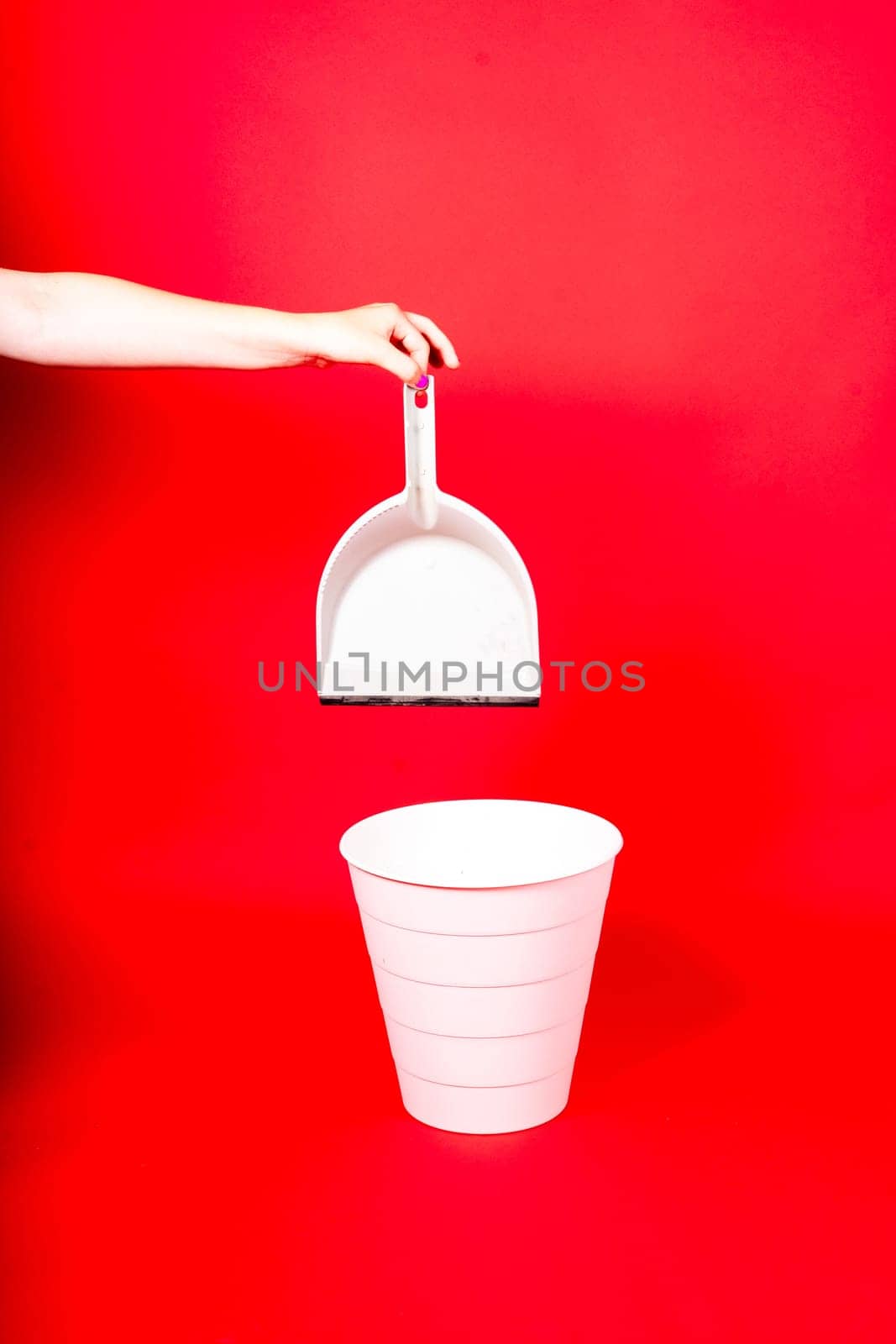 Woman throwing crumpled paper from scoop into rubbish bin on red background by Zelenin