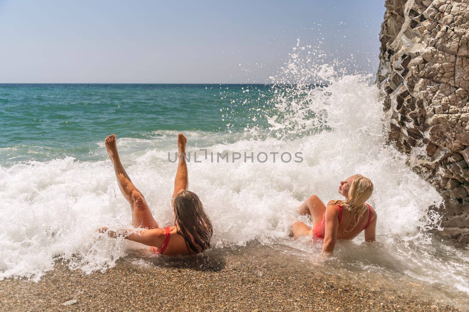 Women ocean play. Seaside, beach daytime, enjoying beach fun. Two women in red swimsuits enjoying themselves in the ocean waves. by Matiunina