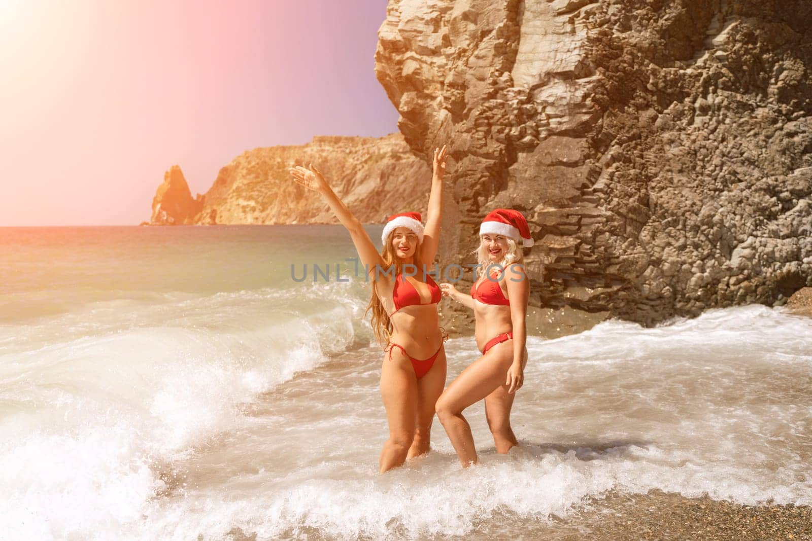 Women in Santa Claus hats run into the sea dressed in red swimsuits. Celebrating the New Year in a hot country by Matiunina
