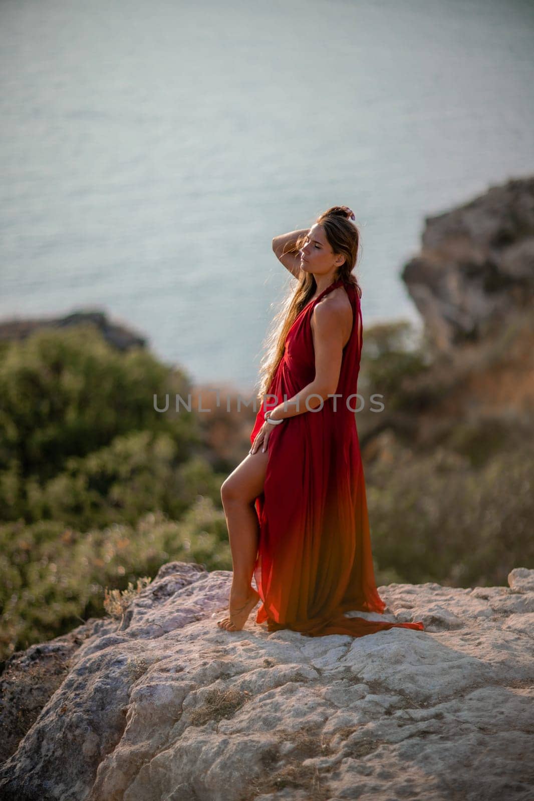 Woman sunset sea red dress, back view a happy beautiful sensual woman in a red long dress posing on a rock high above the sea on sunset. by Matiunina