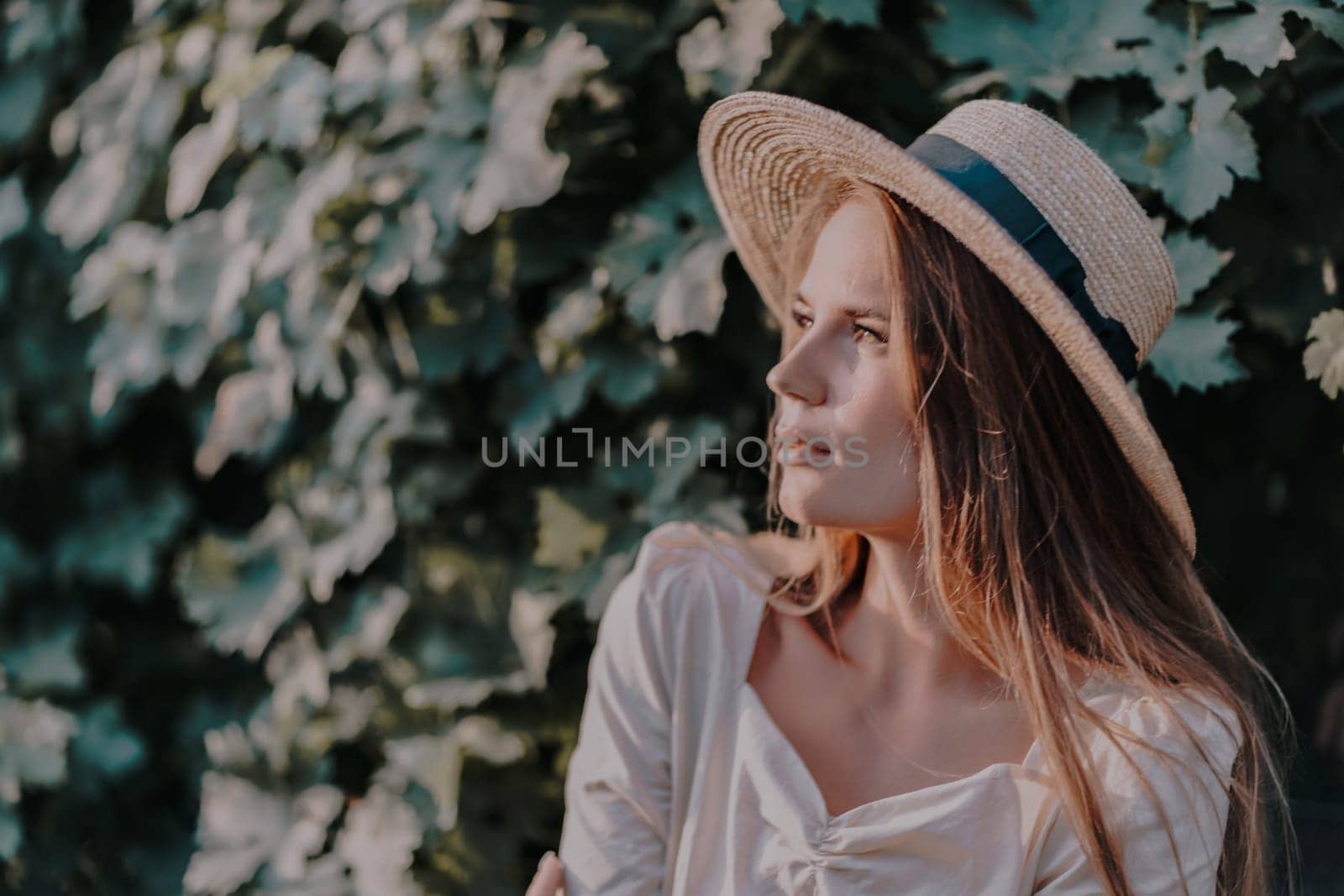 Woman with straw hat stands in front of vineyard. She is wearing a light dress and posing for a photo. Travel concept to different countries.