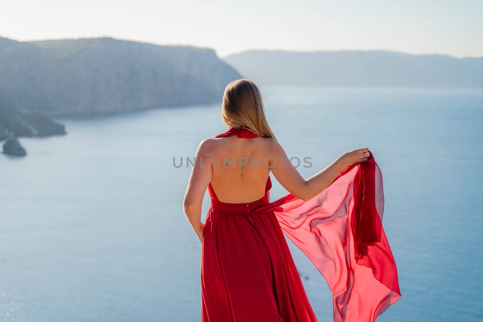 A woman in a red flying dress fluttering in the wind, against the backdrop of the sea