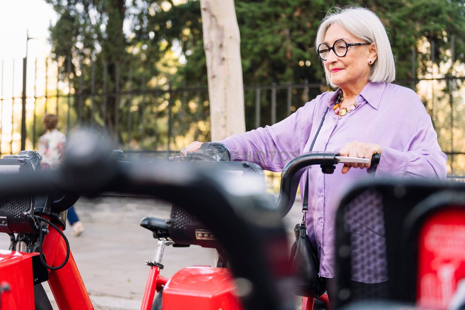 senior woman taking rental bike from parking row, concept of sustainable mobility and active lifestyle in elderly people