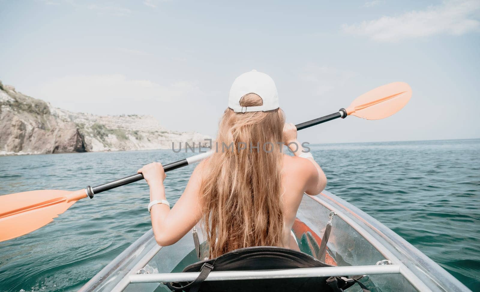 Woman in kayak back view. Happy young woman with long hair floating in transparent kayak on the crystal clear sea. Summer holiday vacation and cheerful female people relaxing having fun on the boat by panophotograph