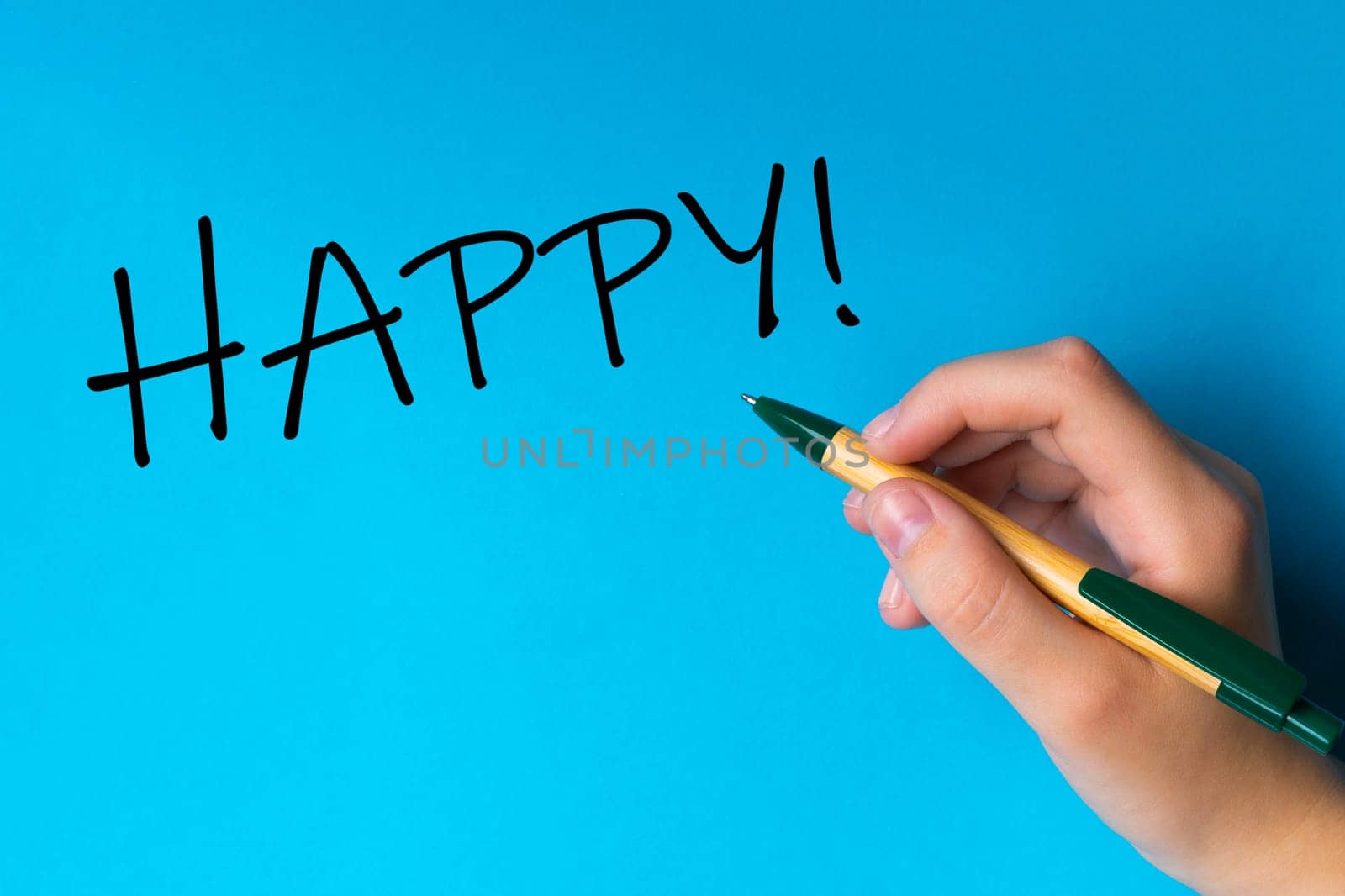 Children hand with pen write on a blue white background. Writing hand. Word HAPPY