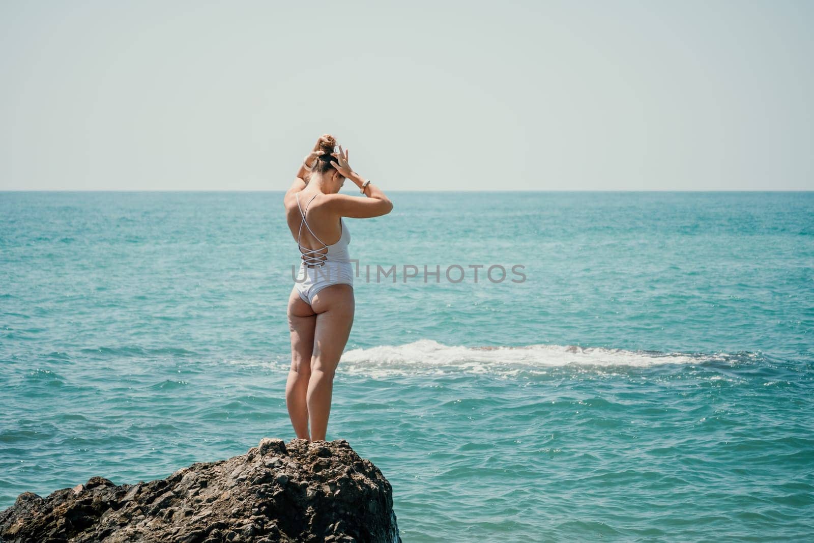 Woman sea yoga. Back view of free calm happy satisfied woman with long hair standing on top rock with yoga position against of sky by the sea. Healthy lifestyle outdoors in nature, fitness concept