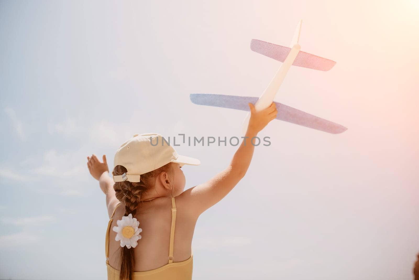 Kid playing with toy airplane. Children dream of travel by plane. Happy child girl has fun in summer vacation by sea and mountains. Outdoors activities at background of blue sky. Lifestyle moment. by panophotograph