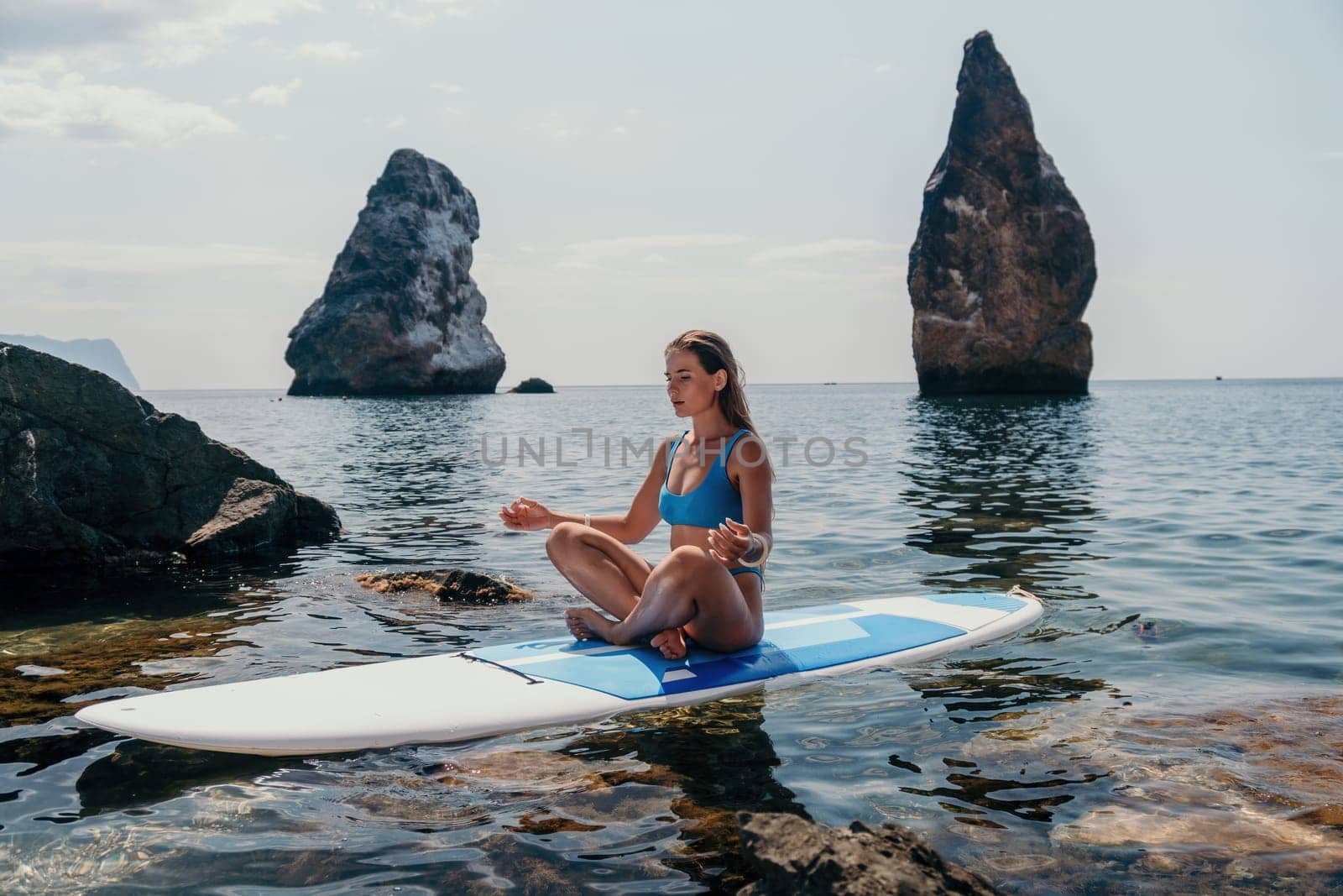 Woman sup yoga. Happy sporty woman practising yoga pilates on paddle sup surfboard. Female stretching doing workout on sea water. Modern individual female hipster outdoor summer sport activity. by panophotograph