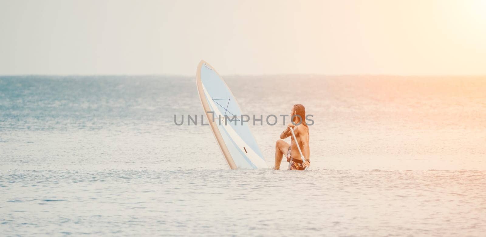 Sea man sup. Asian athlete man swimming in sea and paddleboarding at summer sunset. Healthy strong male enjoy outdoor active lifestyle and water sports on holiday vacation. by panophotograph
