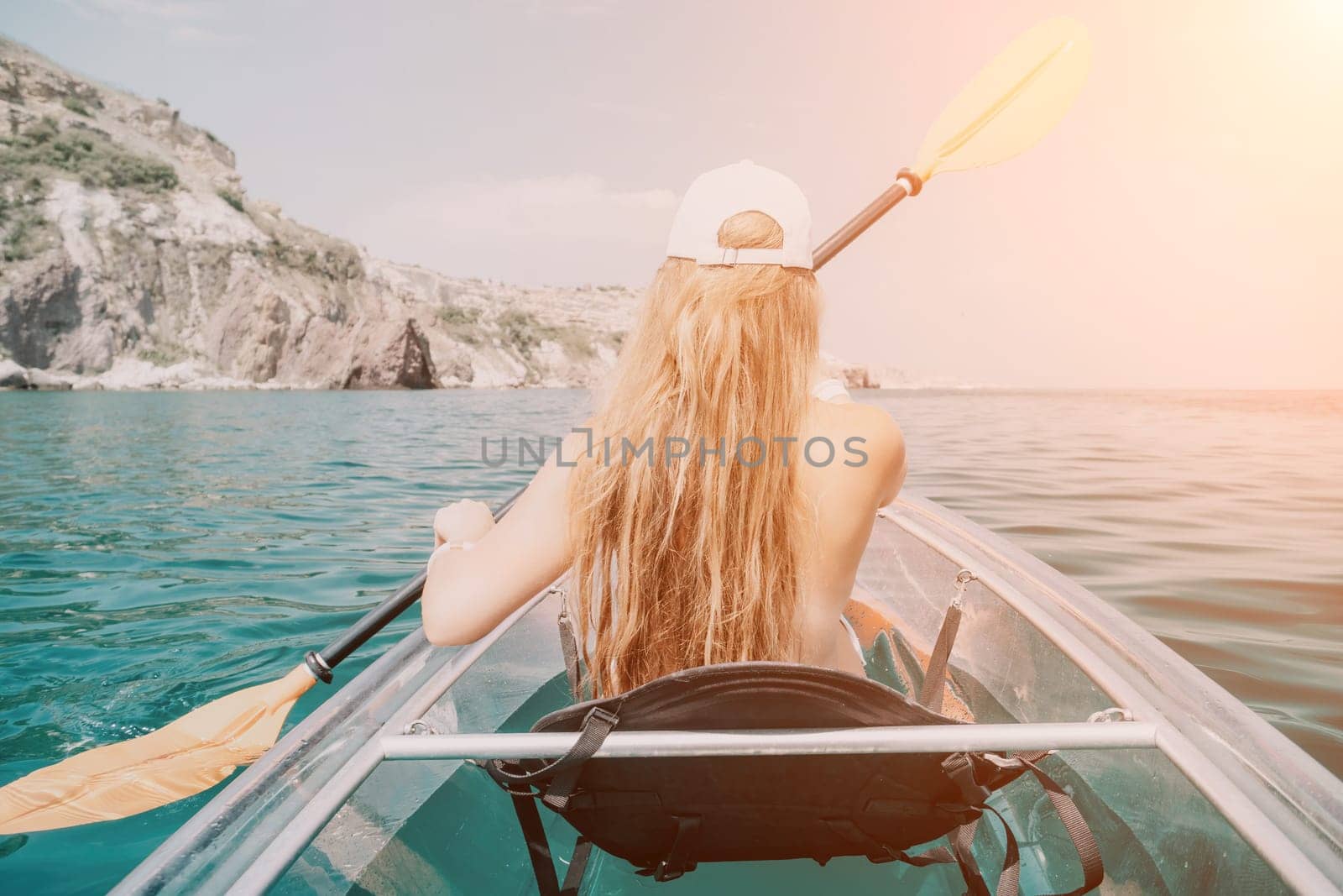 Woman in kayak back view. Happy young woman with long hair floating in transparent kayak on the crystal clear sea. Summer holiday vacation and cheerful female people relaxing having fun on the boat by panophotograph