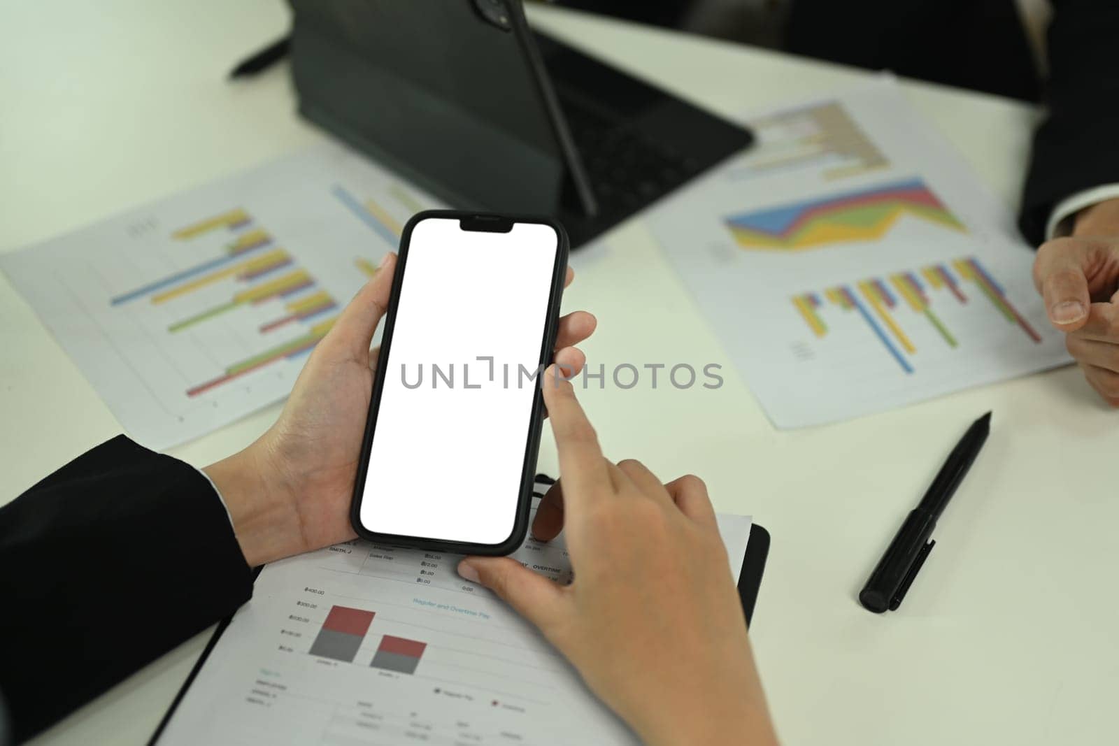 Businesswoman using mobile phone at meeting table with sales statistics documents.