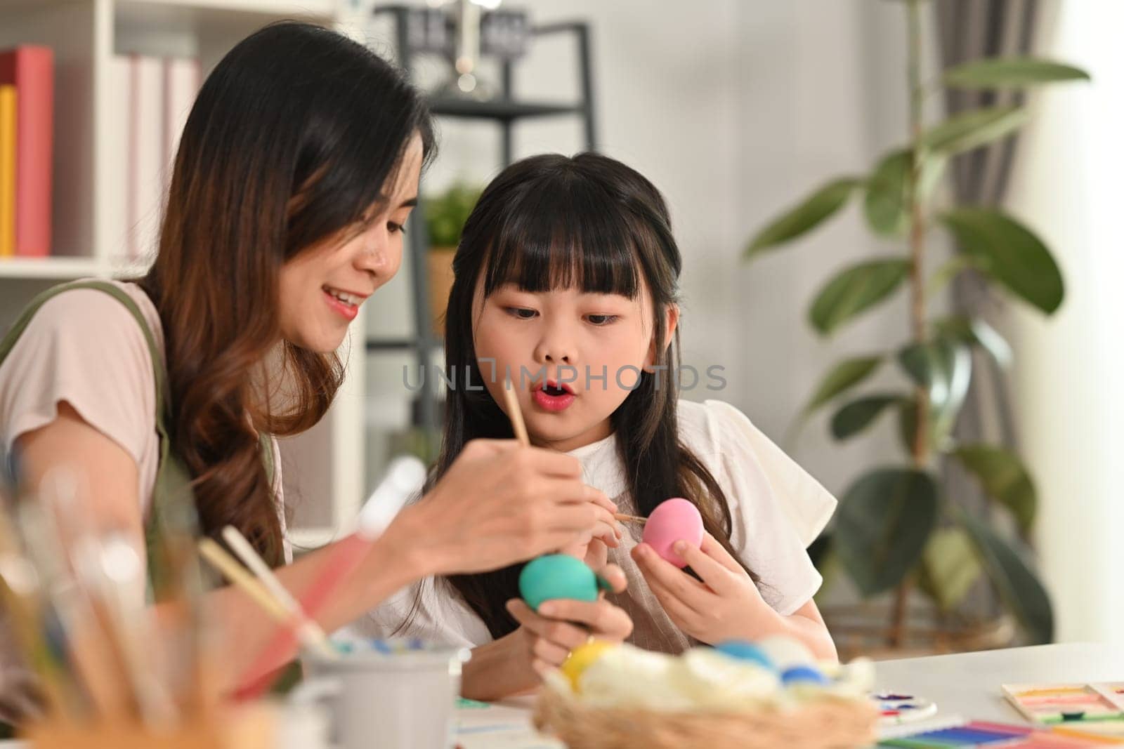 Little girl child girl and her mother painting Easter egg with colorful paints at home by prathanchorruangsak