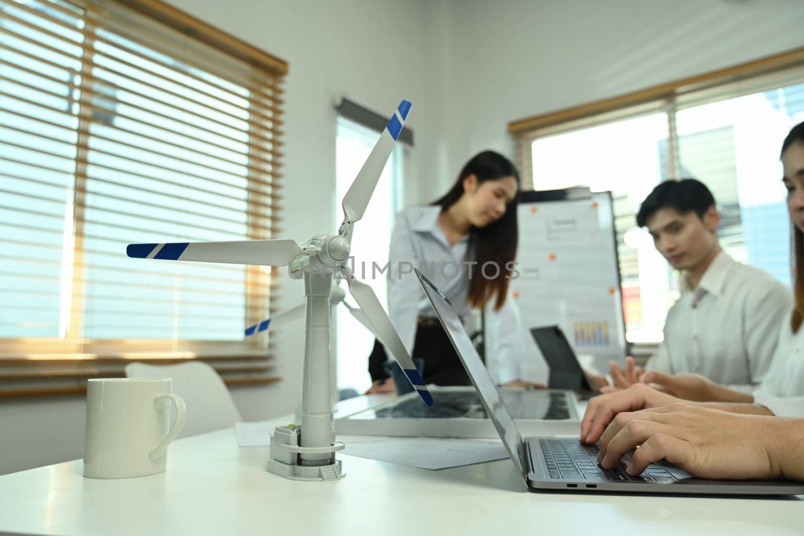 Wind turbine model on a meeting table with business people brainstorming project in background