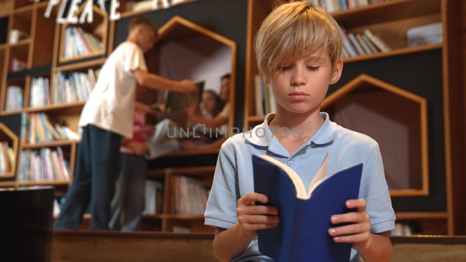 Attractive boy reading book while group of students learning behind. Erudition. by biancoblue