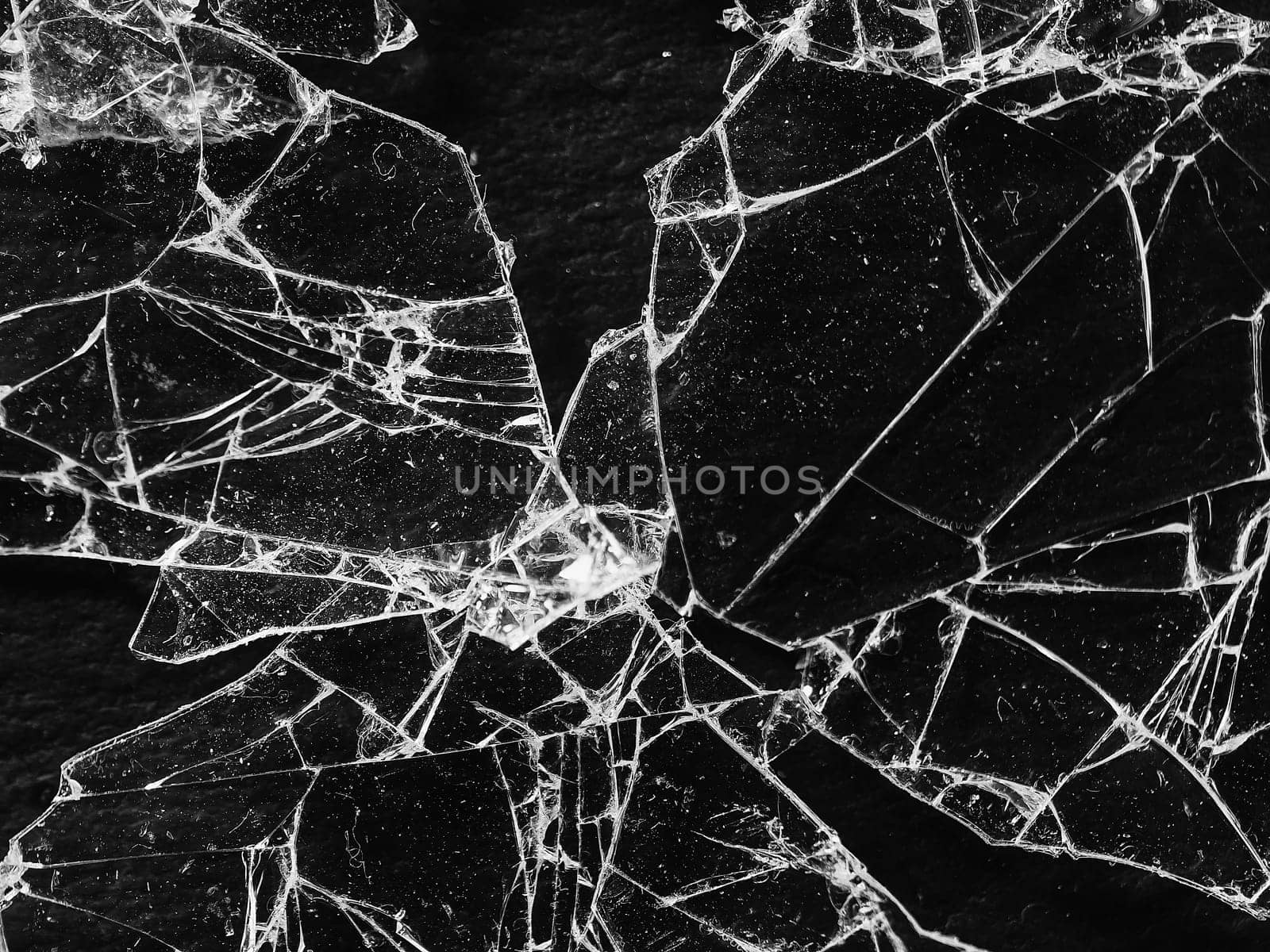 Shards of broken glass on a dark background reflecting highlights, chaotically scattered, some overlapping. Fractures and chips visible in places. Creates a sense of fragility and breaking apart into pieces.