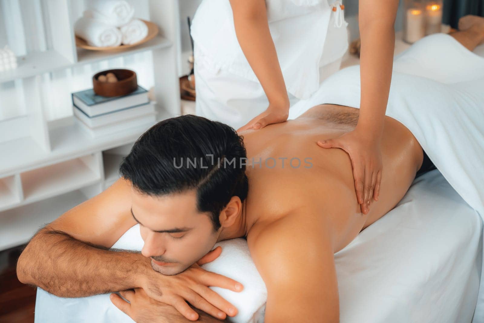 Caucasian man customer enjoying relaxing anti-stress spa massage and pampering with beauty skin recreation leisure in day light ambient salon spa at luxury resort or hotel. Quiescent