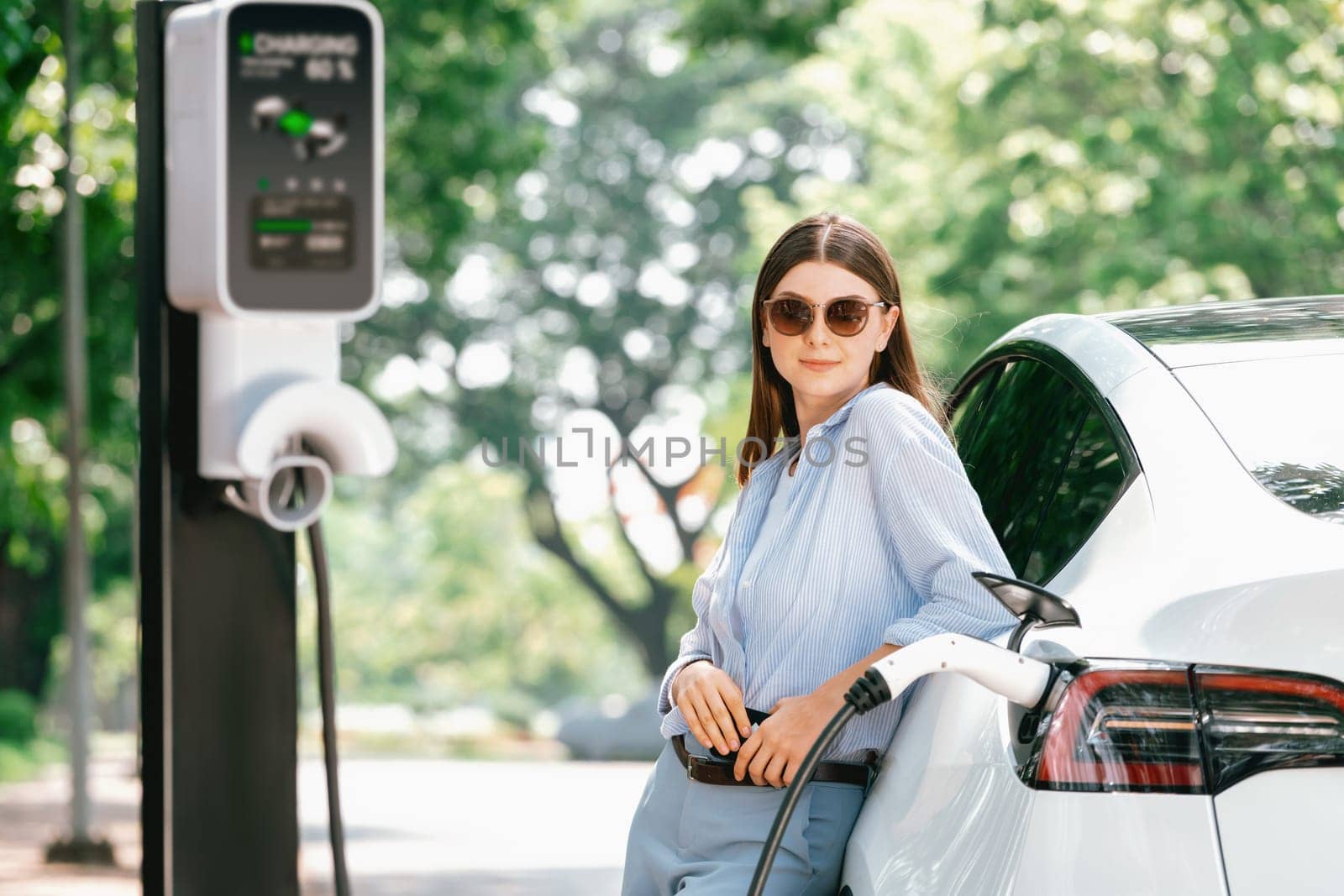 Young woman recharging battery for electric car during road trip. Exalt by biancoblue