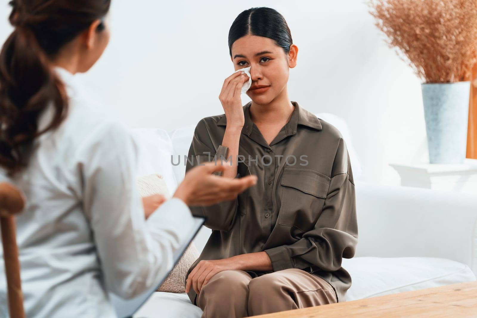 Sad PTSD woman patient in uttermost therapy for mental health with psychologist, depression or grief after life failure. Frustrated trauma young woman talking to a psychologist about emotion in clinic