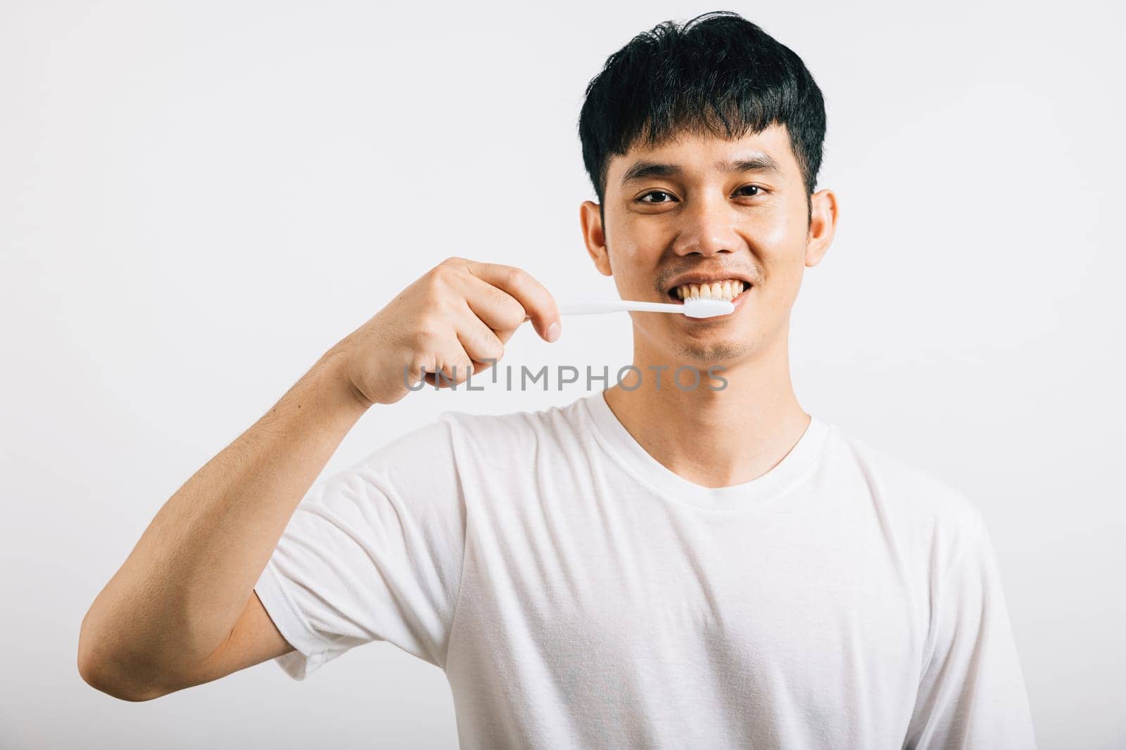 A confident Asian teenager promotes dental health by brushing his teeth with a smile. Studio shot isolated on white, emphasizing dental care and oral hygiene.