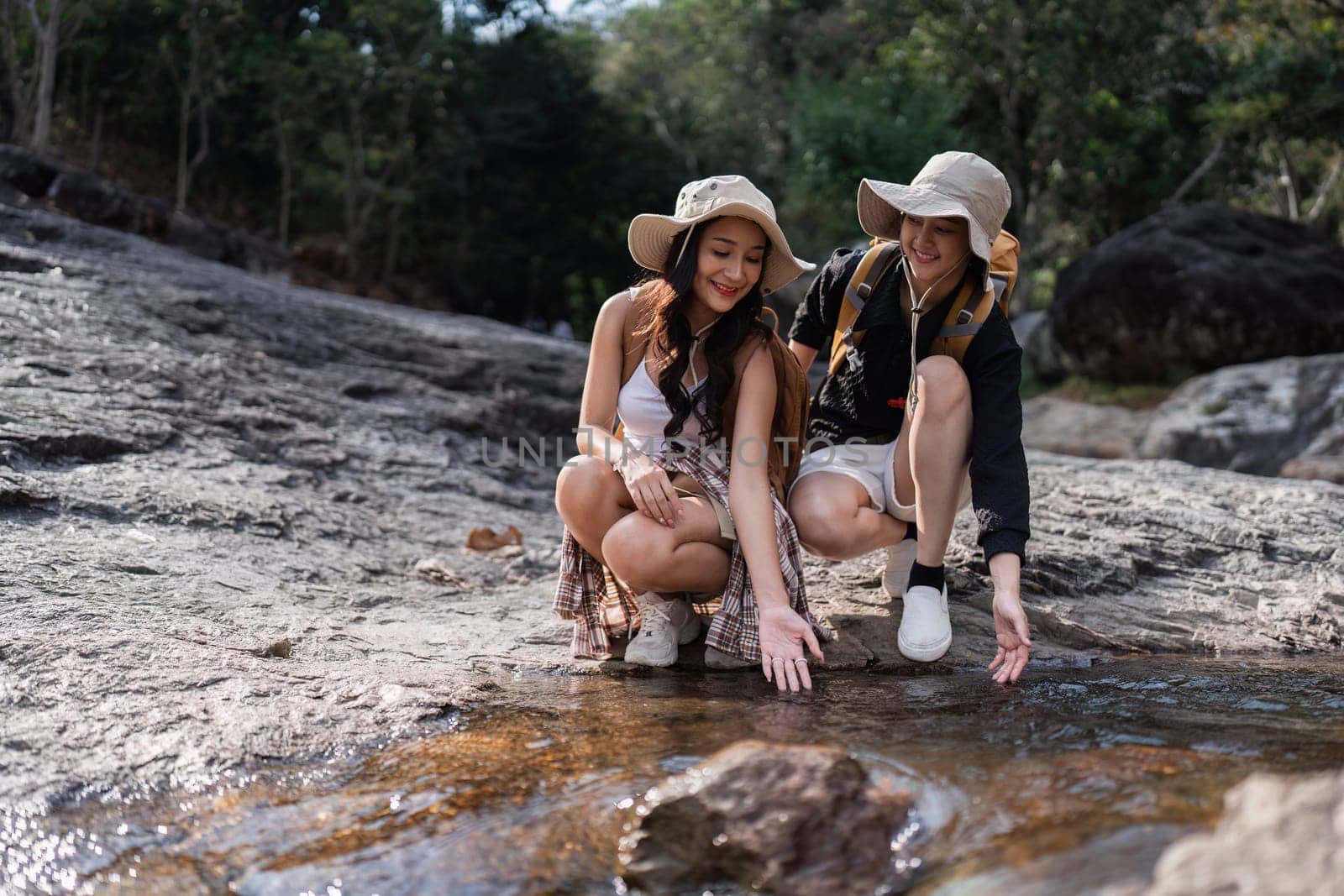 Happy LGBT Lesbian couple Travelers Hiking with Backpacks in waterfall Trail. LGBT Lesbian Couple Hikers with backpacks walks in mountains in vacation by itchaznong