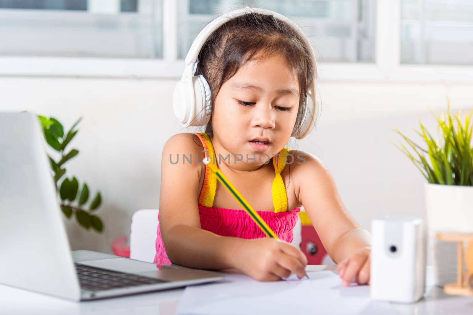 Little kid preschool wear headphone sit at desk use laptop computer and communicates on Internet online video call with teacher, Asian child girl study video conference distant education at home