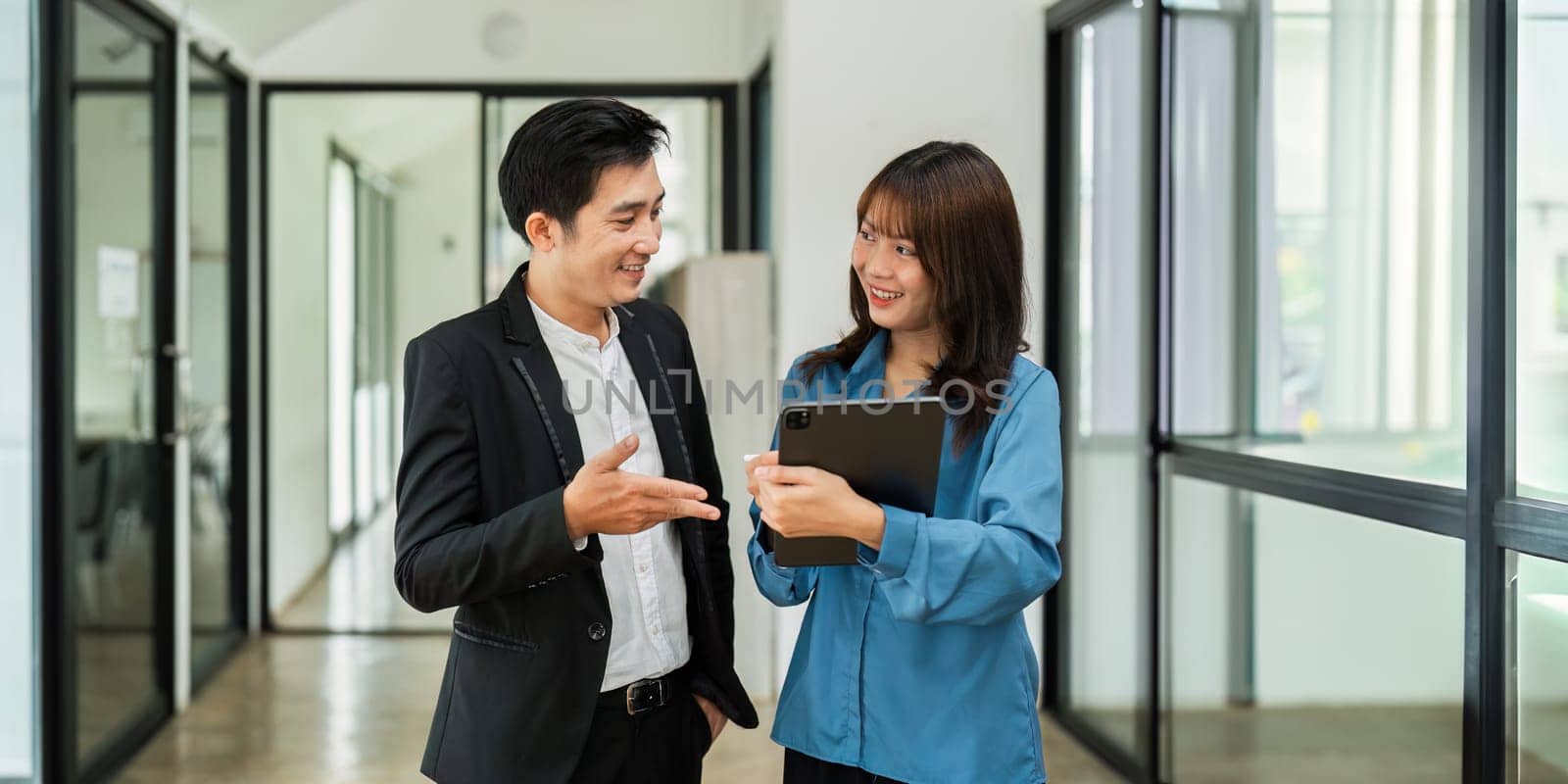 Asian woman and business man working using digital tablet tech discussing financial market data standing at corporate office by itchaznong