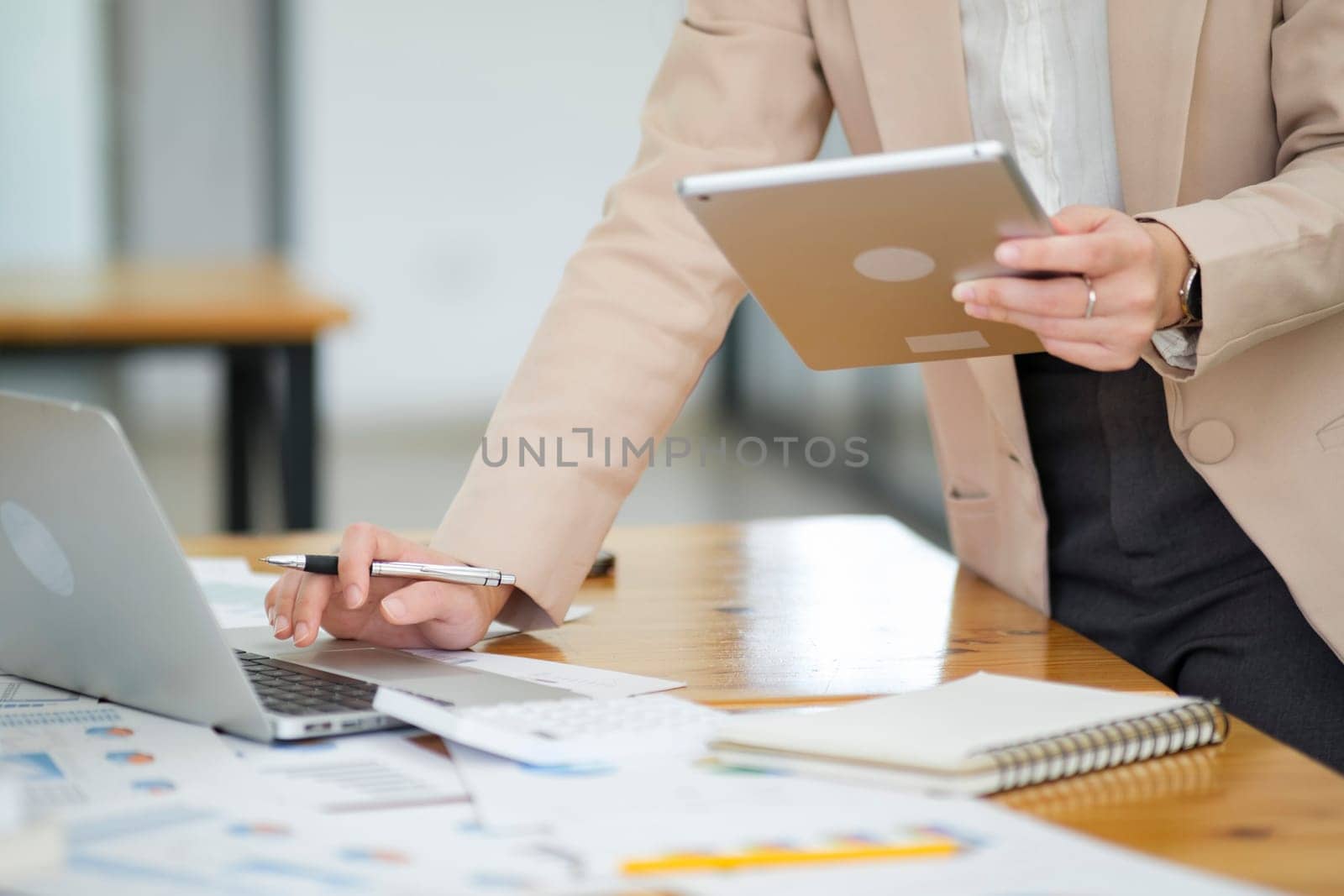 Close-up of a businesswoman hand as she meticulously analyzes data on her laptop, surrounded by business charts and a calculator..