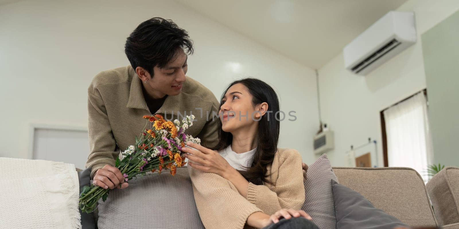 Romantic young asian couple embracing with holding flowers and smiling in living room at home. fall in love. Valentine concept by nateemee