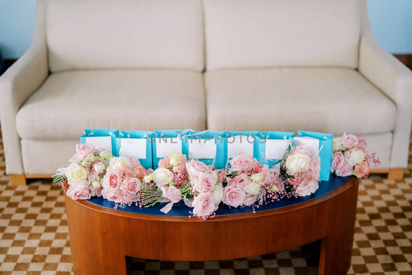 Small bouquets of pink roses lie on the table near blue gift bags in the room. High quality photo
