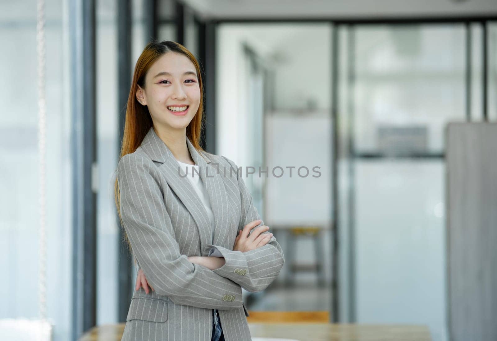 A professional and confident businesswoman smiling at the camera, standing by her desk with a laptop in a modern office.