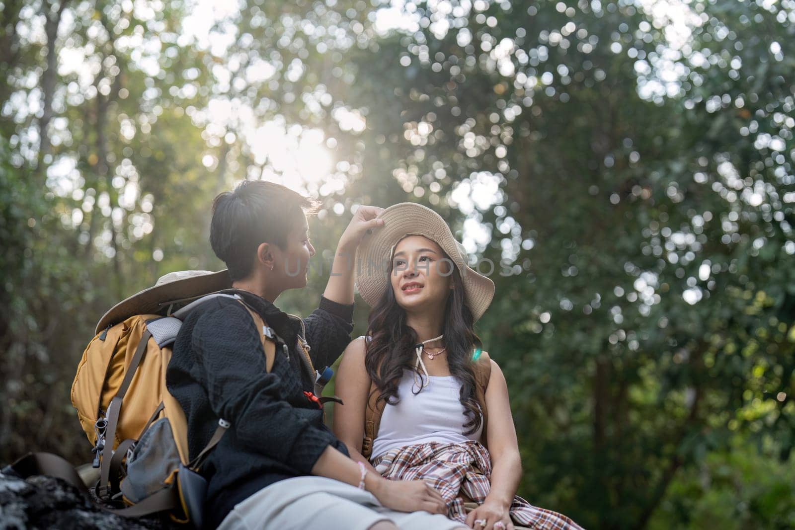 Cheerful romantic lesbian couple traveler with backpacks on their backs go hiking through the forest and siting relaxing while hiking in the mountains by nateemee