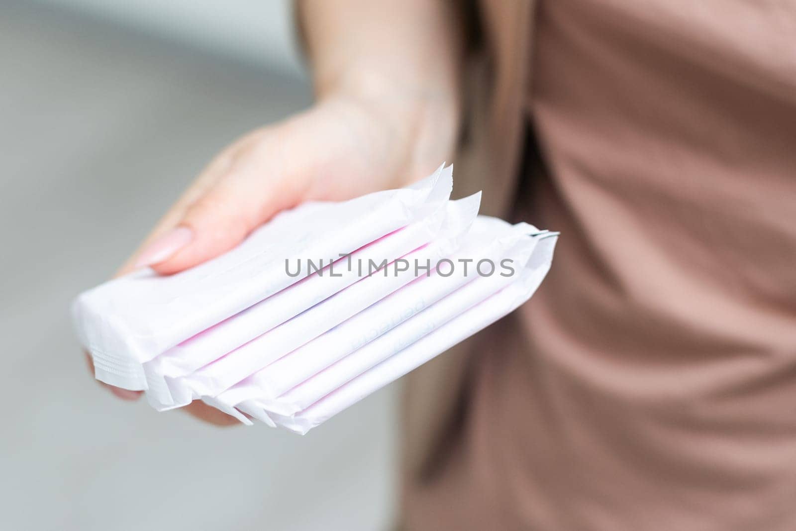 Young adult woman hand holding packs of sanitary towel on light background. Pastel color. Closeup. Empty place for text. High quality photo