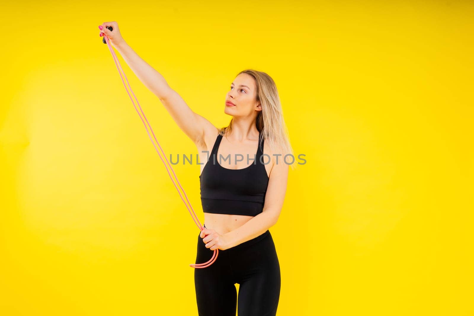 Fitness woman doing jumping exercises with a skipping rope on colorful yellow red background.