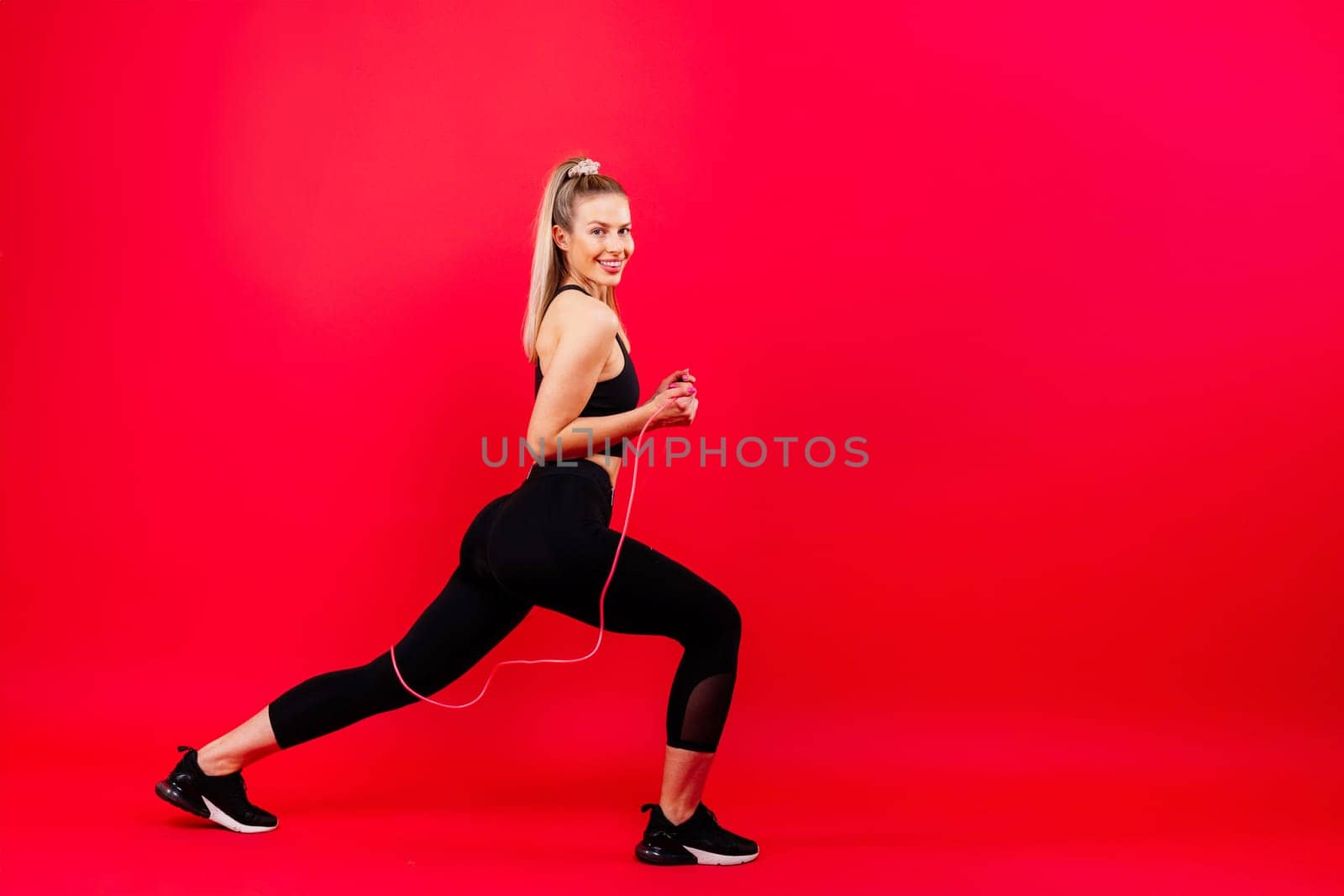 Fitness woman doing jumping exercises with a skipping rope on colorful yellow red background.