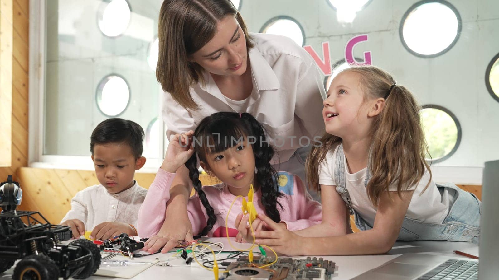 Teacher looking at children while diverse student looking at screen. Children excited in presentation while drawing or writing art books at table with toys and color pencil placed on table. Erudition.
