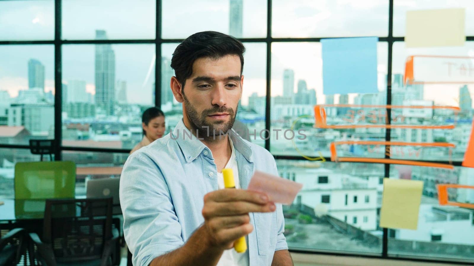 Smart project manager writing sticky notes and mind mapping at glass wall to planing strategy while multicultural businesspeople discussing about business plans at office with city view. Tracery