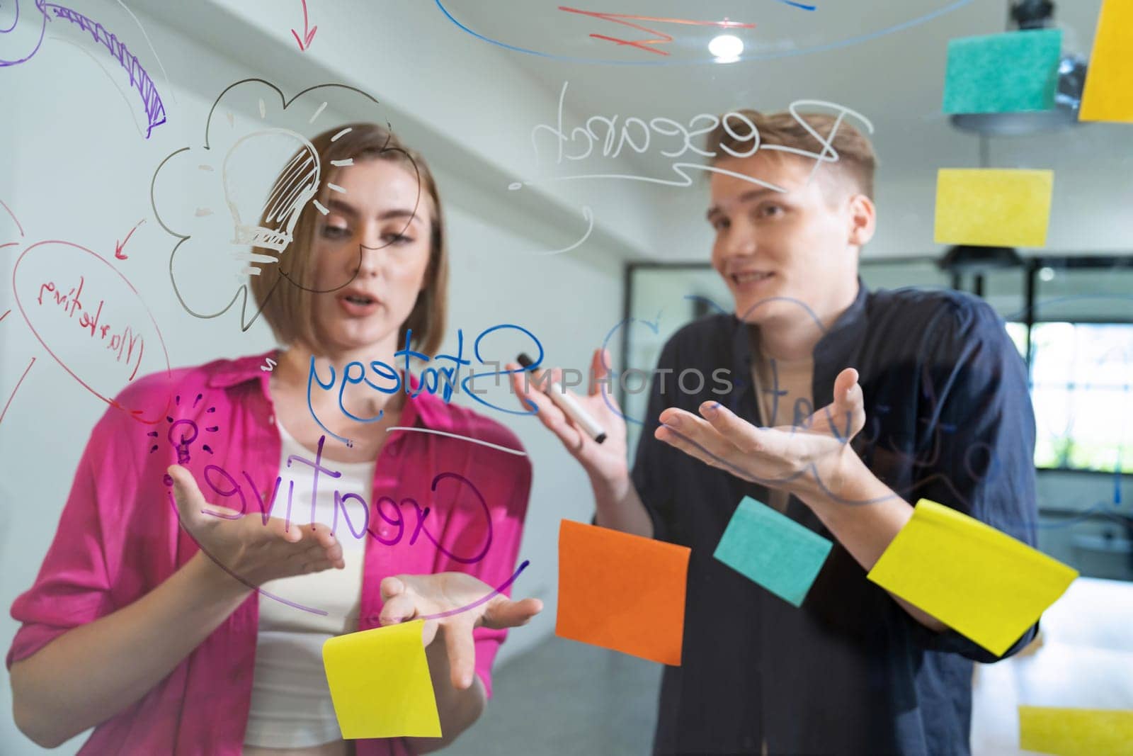 Couple of businesspeople discussing and brainstorming about solving marketing problem in front of glass board at business meeting by using mind map and sticky notes. Working together. Immaculate.