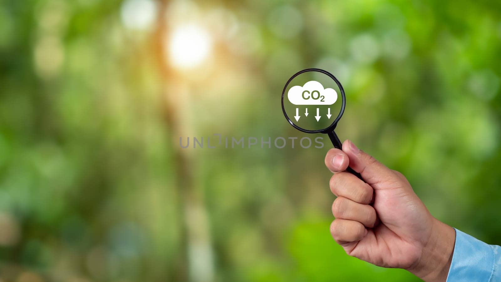 A clean and friendly environment without carbon dioxide emissions, Hand holding magnifying glass with CO2 reduction icon inside, carbon credit to limit global warming from climate change, carbon neutral. by Unimages2527