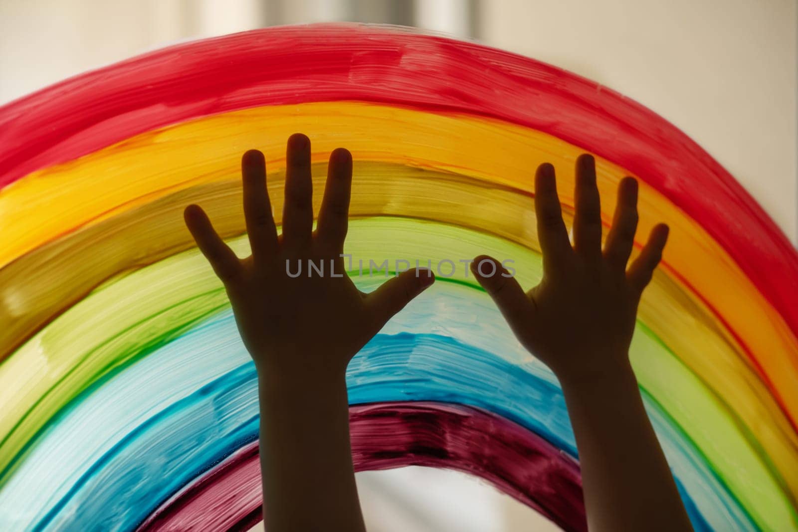 Child's hands touch painting rainbow on a window