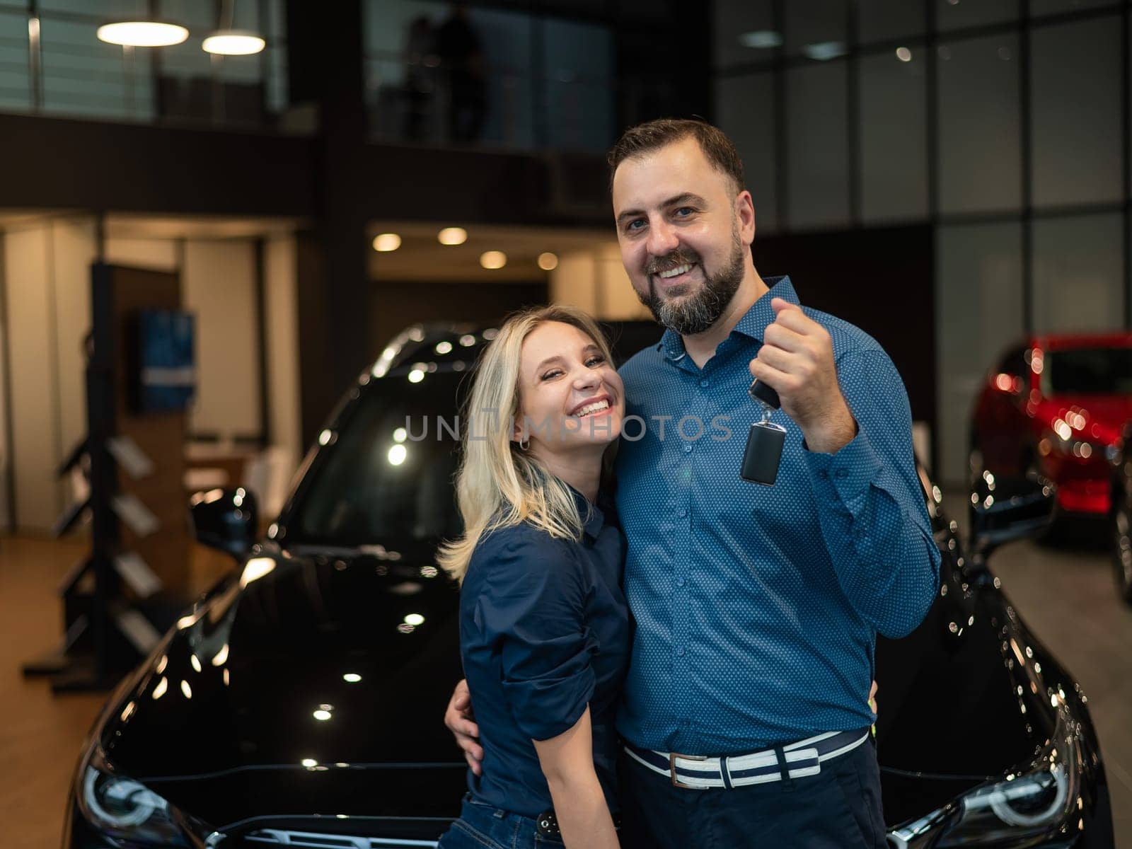 Happy caucasian couple hugging and man holding new car keys in car showroom. by mrwed54