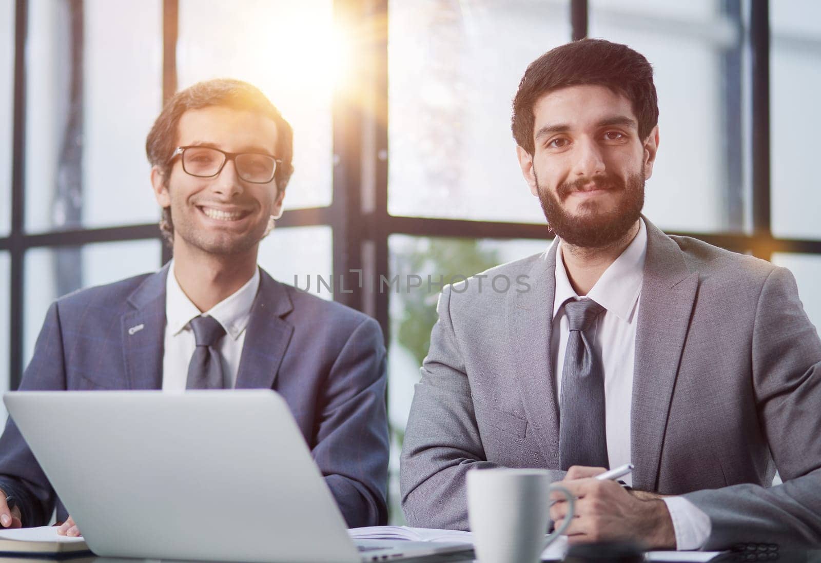 two businessmen are sitting at the table in the office and looking at the camera
