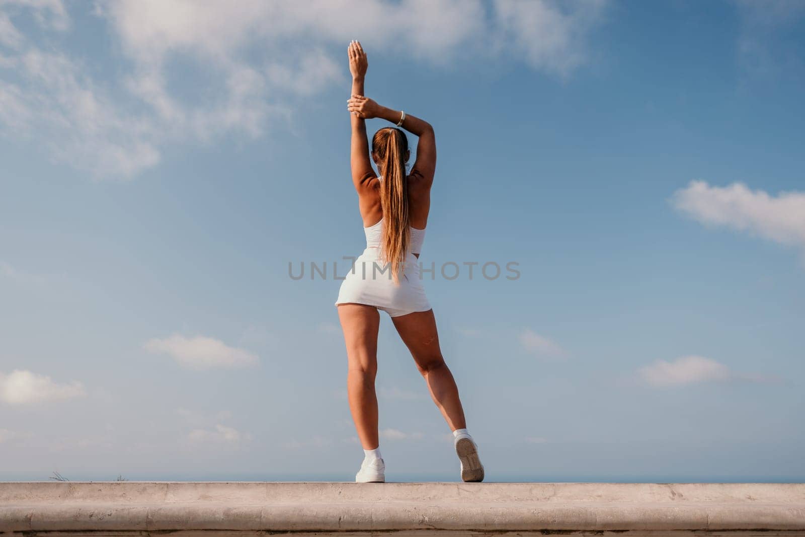 Fitness woman sea. Active, happy middle-aged woman in white sportswear exercises outdoors in a park over sea. Healthy lifestyle, physical activity and female fitness pilates and yoga routines. by panophotograph